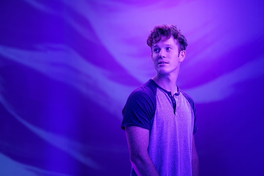 A person standing against a purple background looks into the distance.