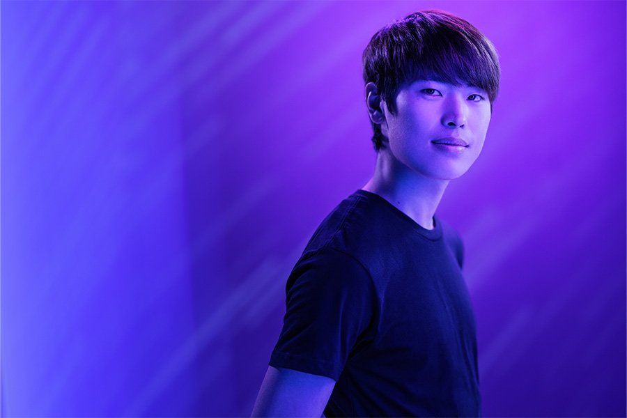 A person with purple lighting looks off camera.